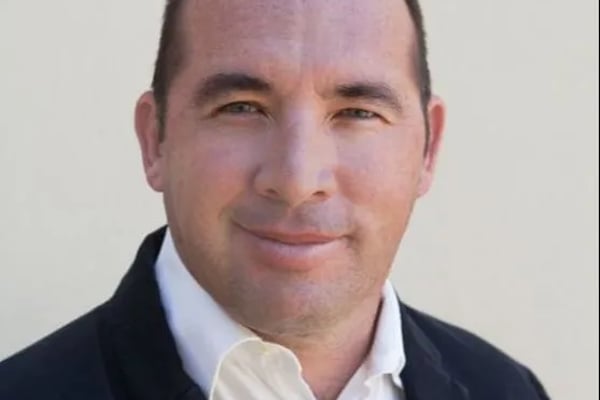 Headshot of man in dark blazer and white shirt against neutral background