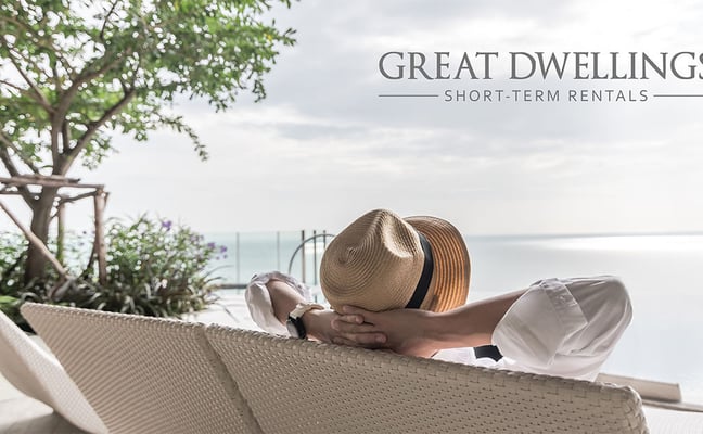 Person in straw hat relaxing in lounge chair overlooking calm water and tropical garden